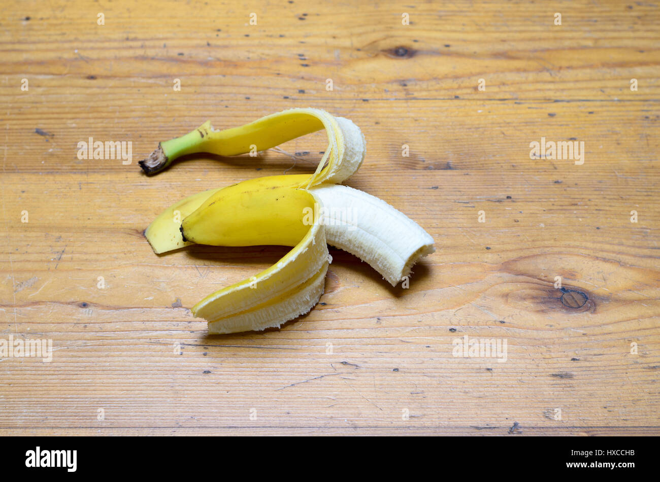 Parzialmente pelato mezze mangiate Giallo maturo banana per un delizioso snack sani giacente nel mezzo di un tavolo di legno con copia spazio, ad alto angolo di visione Foto Stock