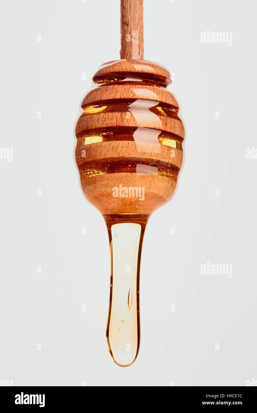 Cucchiaia di miele con miele di gocciolamento su sfondo bianco Foto Stock