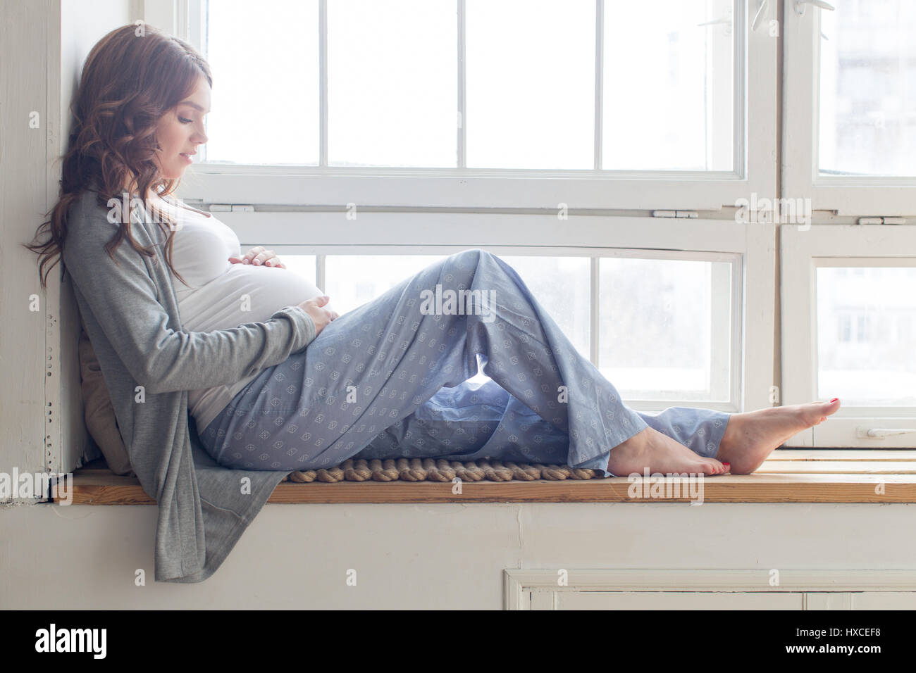 Donna incinta è seduta sul davanzale Foto Stock