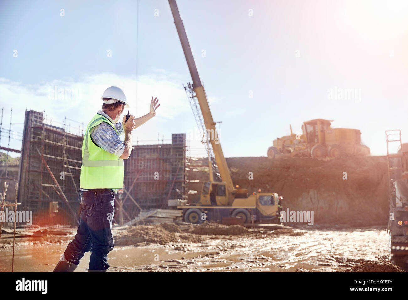 Operaio edile foreman utilizzando un walkie-talkie dirigere gru a sunny sito in costruzione Foto Stock