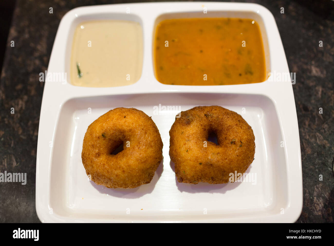 Croccante di sud indiane colazione vada con chutney e sambar su un bianco piastra partizionata Foto Stock
