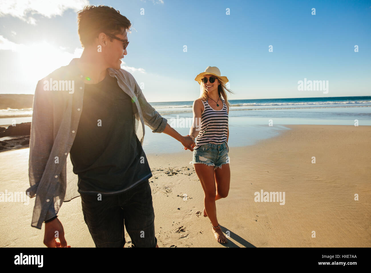 Colpo all'aperto di romantica coppia giovane tenendo le mani e camminando sulla spiaggia. Giovane uomo e donna che cammina sulla riva del mare in un giorno di estate. Foto Stock