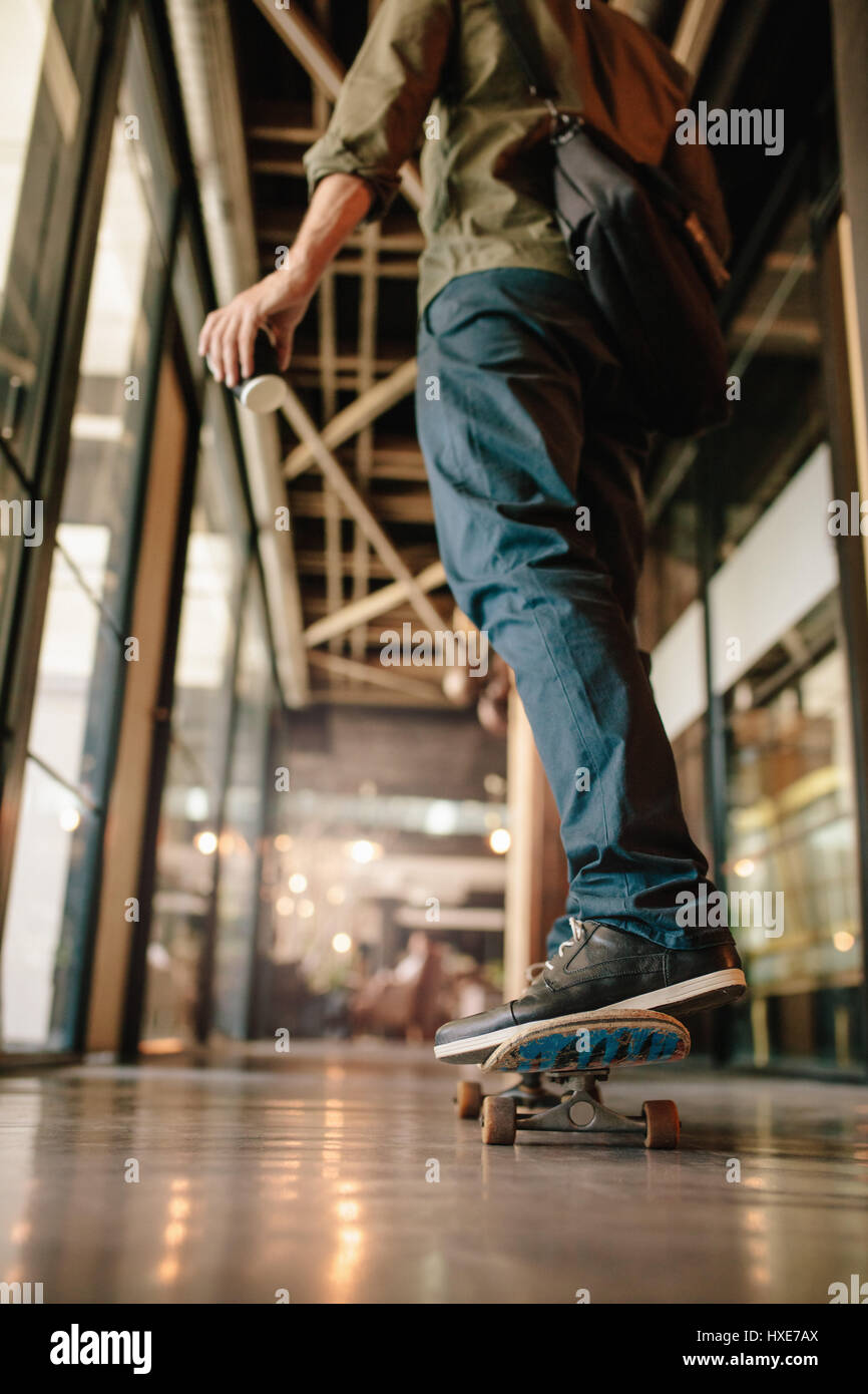 Vista posteriore del colpo di uomo skateboarding in ufficio corridoio. Giovane imprenditore pattinaggio attraverso il suo ufficio di avvio. Foto Stock