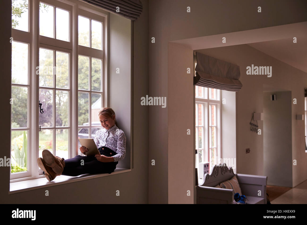 La ragazza si siede da finestra a casa utilizzando la tavoletta digitale Foto Stock