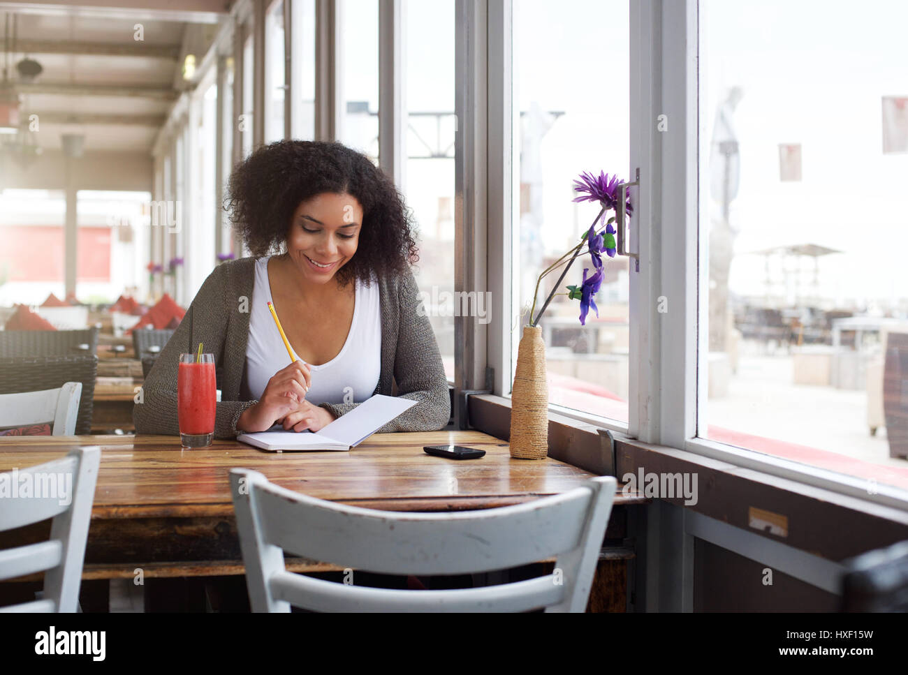 Ritratto di un sorridente african american studentessa iscritto nel libro presso il cafe Foto Stock