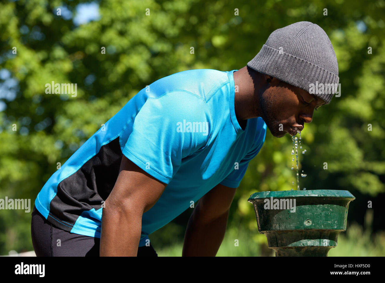 Lato ritratto di un giovane uomo nero acqua potabile da una fontana di acqua nel parco pubblico Foto Stock