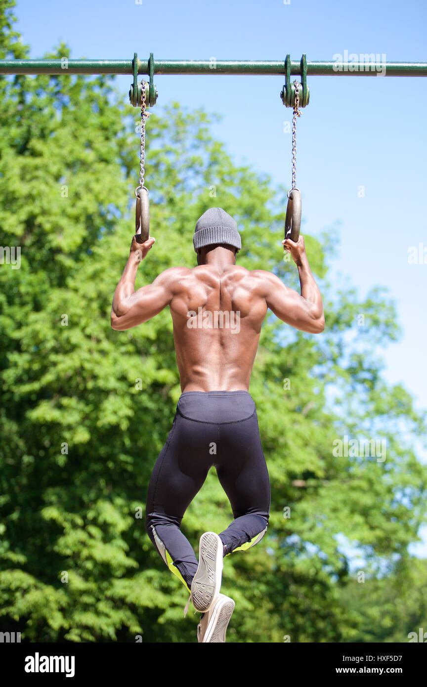 Strong African American uomo tirando verso l'alto su anelli ginnasta al di fuori Foto Stock