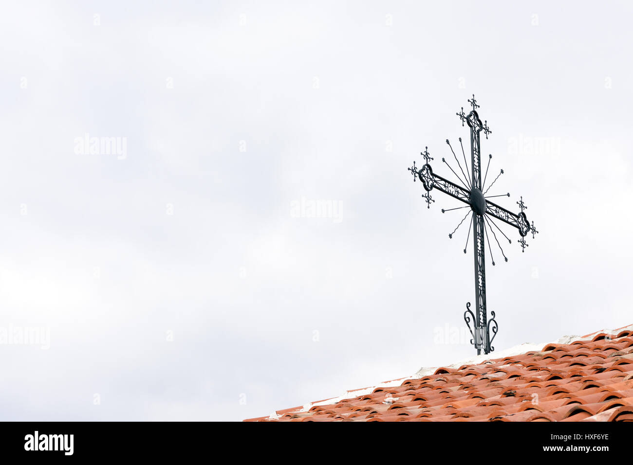 Sfondo religioso della croce di ferro rosso sul tetto di tegole contro il cielo nuvoloso con spazio di copia Foto Stock