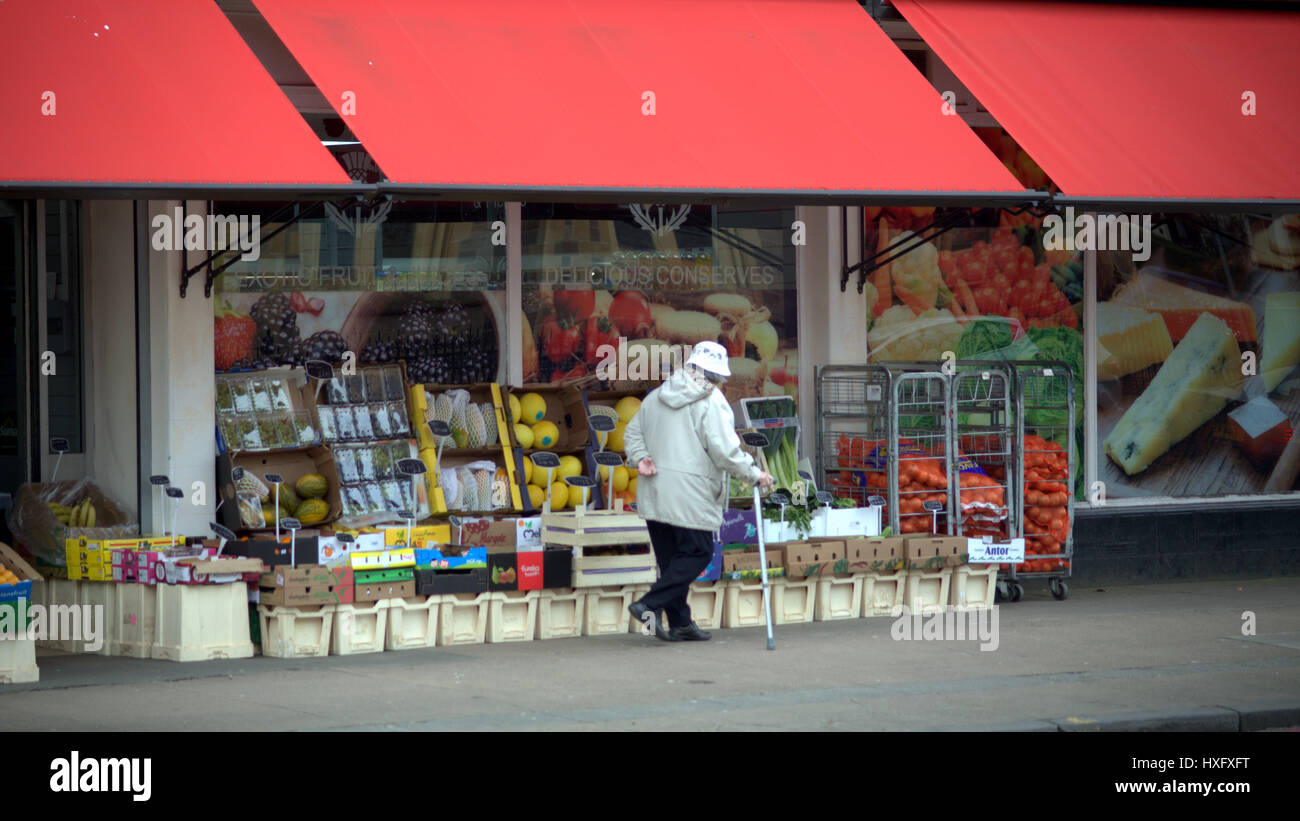 Ol'd donna cinese con la schiena rotta e bastone al di fuori del negozio di frutta Foto Stock