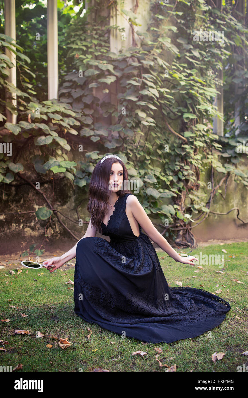 La ragazza con i capelli lunghi che indossa un abito nero, tenendo uno specchio Foto Stock