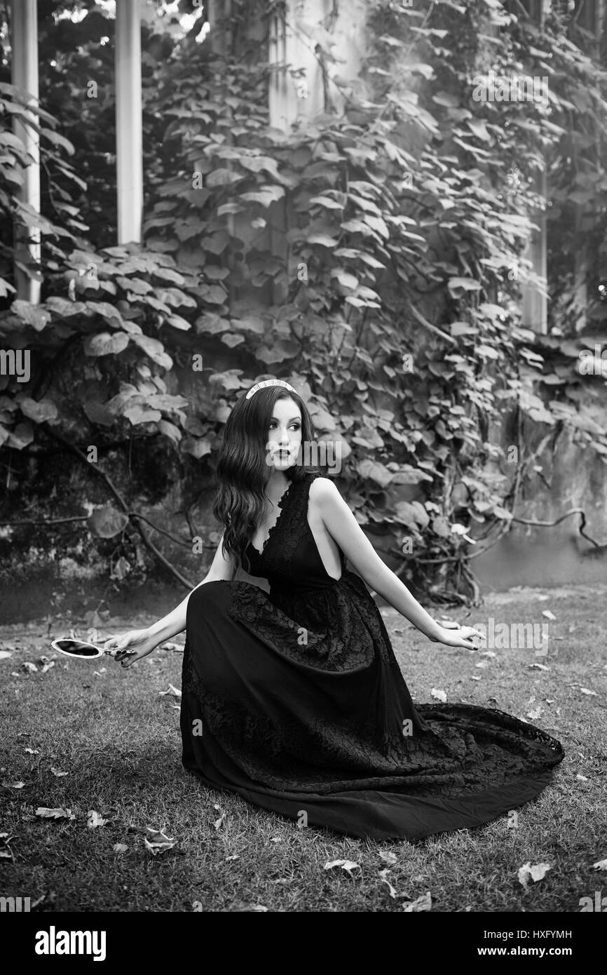 La ragazza con i capelli lunghi che indossa un abito nero, tenendo uno specchio Foto Stock