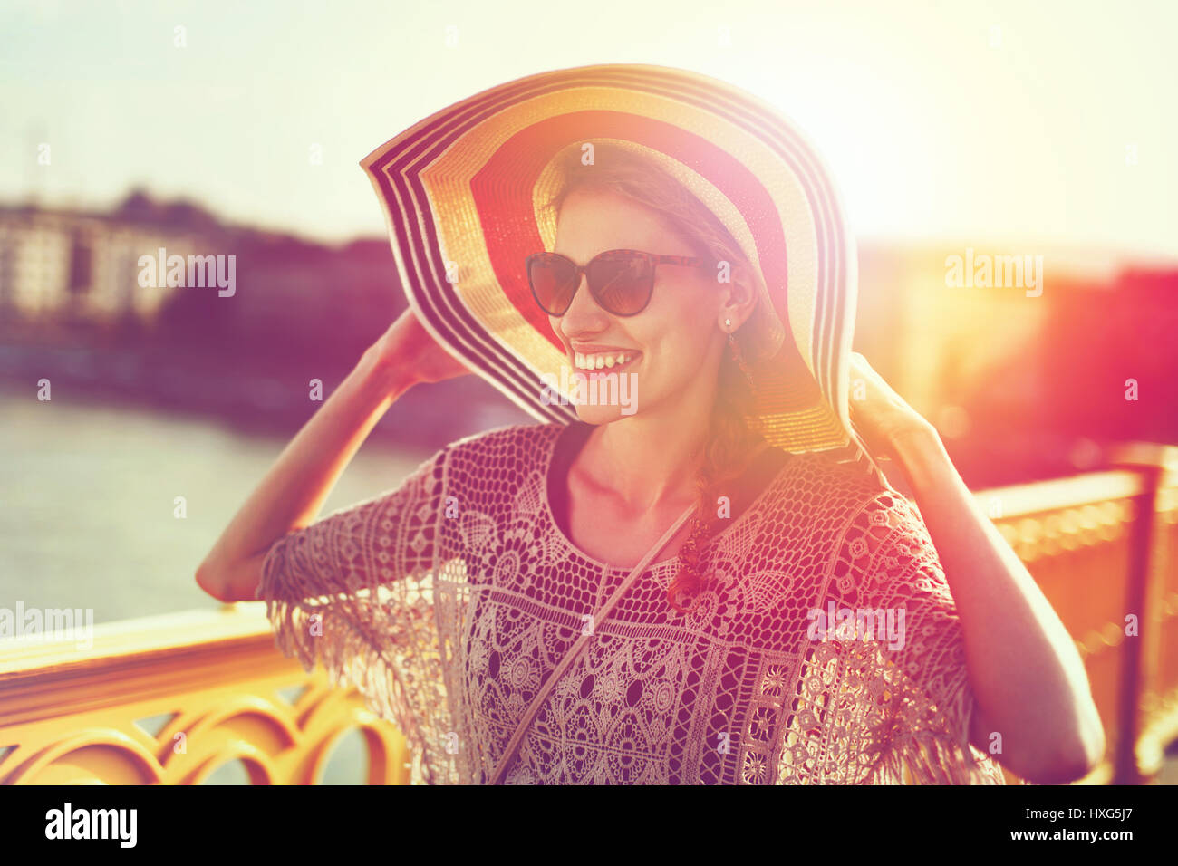 Felice giovane donna in hat camminando sul ponte in sunset, positività Foto Stock