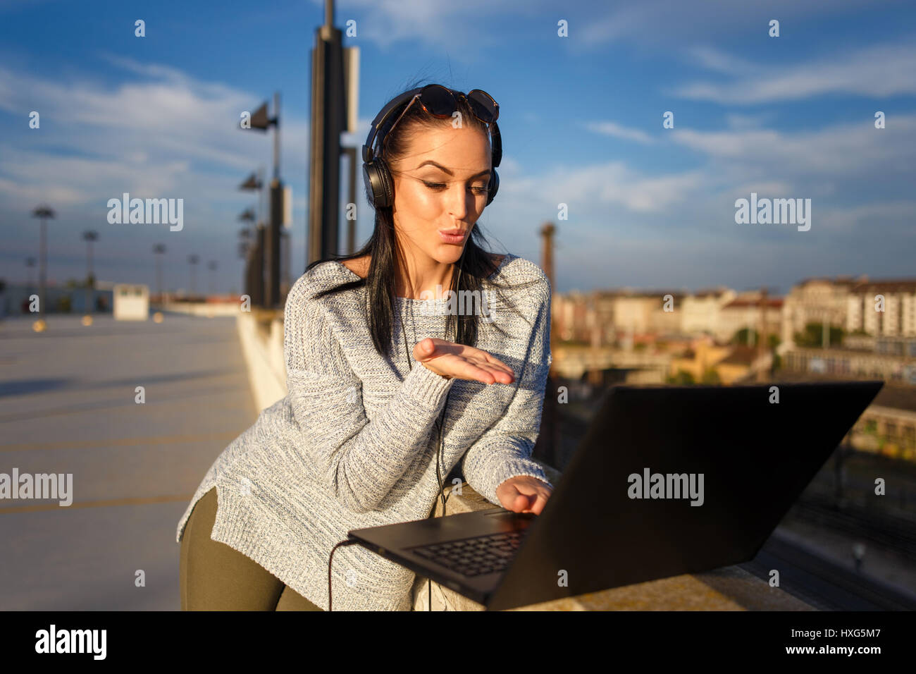 Giovane donna invio baci dal computer portatile all'aperto, tecnologia wireless Foto Stock