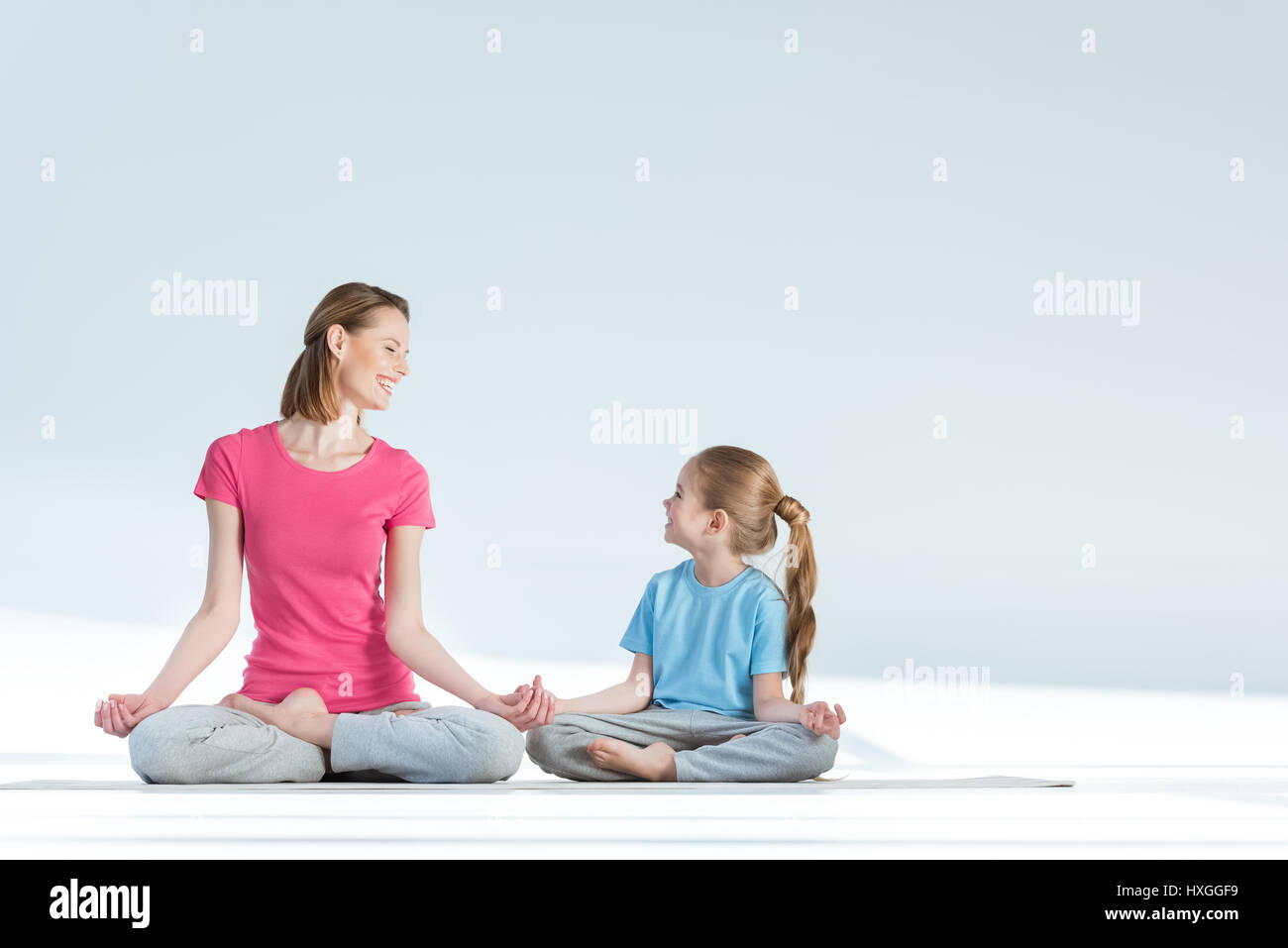 Sportivo sorridente madre e figlia la pratica posizione del loto con gyan mudra asana su bianco Foto Stock