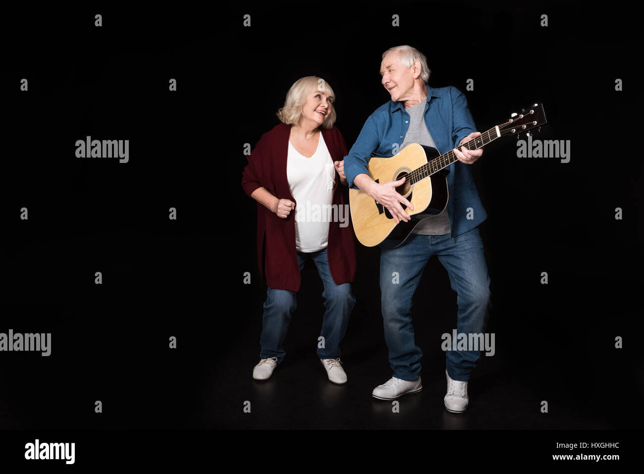 Senior uomo a suonare la chitarra mentre woman dancing vicino a y su nero Foto Stock
