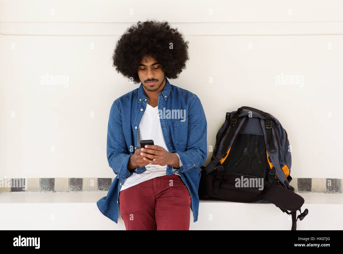 Ritratto di un fresco travel ragazzo seduto con il telefono cellulare ed il sacchetto Foto Stock