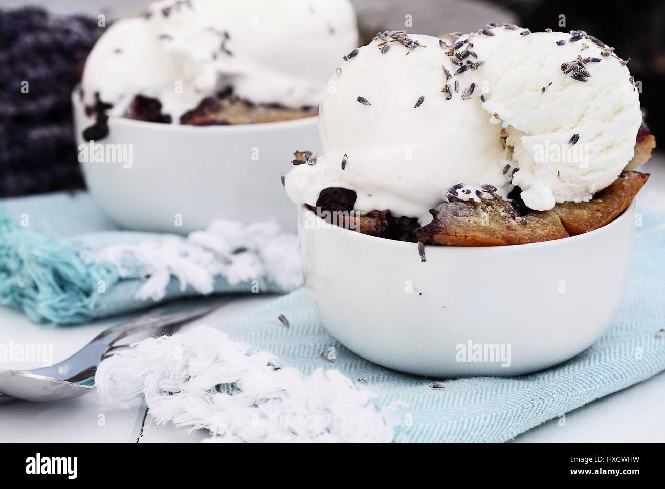 Due ciotole di pane appena sfornato in casa mirtillo lavanda cobbler guarnita con gelato alla vaniglia. Messa a fuoco selettiva sul piatto in primo piano con estrema deve Foto Stock