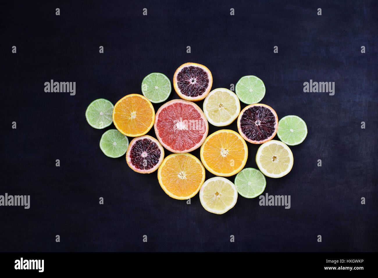 Varietà di agrumi (arancione, sangue arance, limoni, pompelmi e limes) oltre un nero sfondo rustico. Immagine ripresa dalla testa. Foto Stock