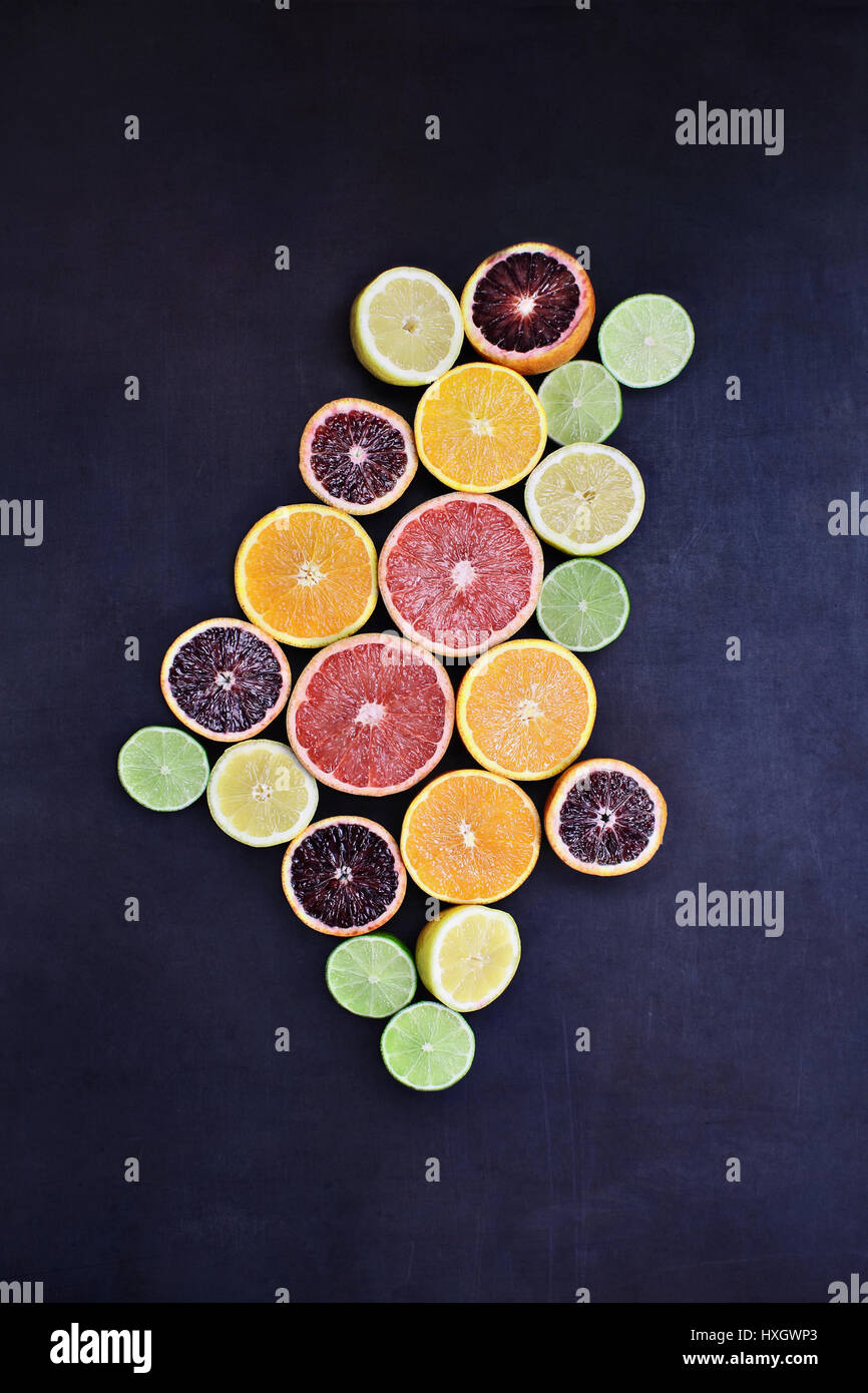 Varietà di agrumi (arancione, sangue arance, limoni, pompelmi e limes) oltre un nero sfondo rustico. Immagine ripresa dalla testa. Foto Stock