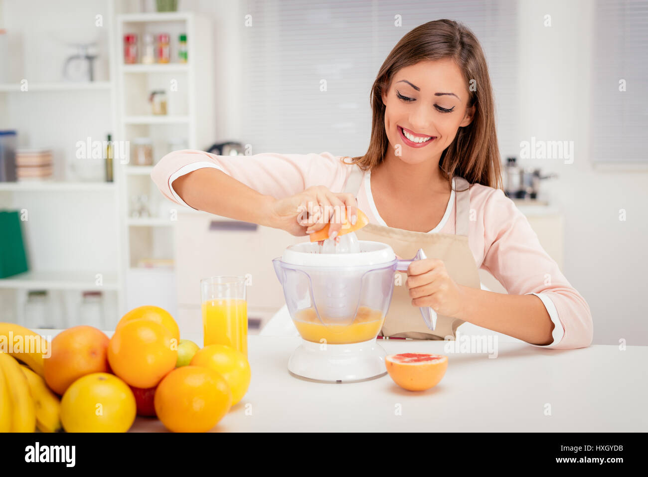 Bella giovane donna in cucina spremendo il succo d'arancia con un spremiagrumi elettrico. Foto Stock