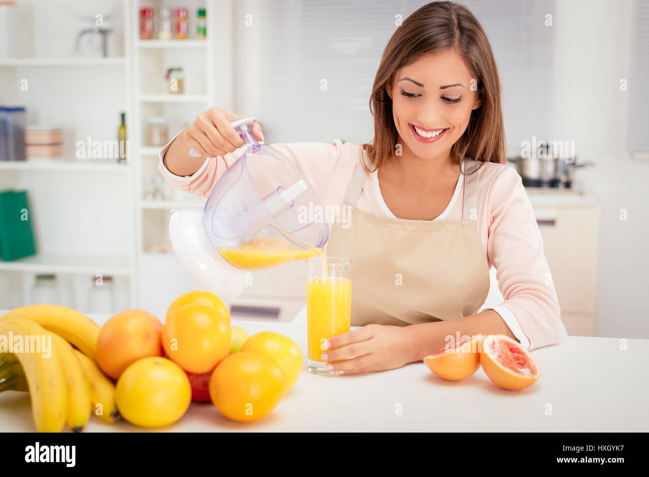 Bella giovane donna in cucina spremendo il succo d'arancia con un spremiagrumi elettrico. Ella è succo di versare in un bicchiere. Foto Stock