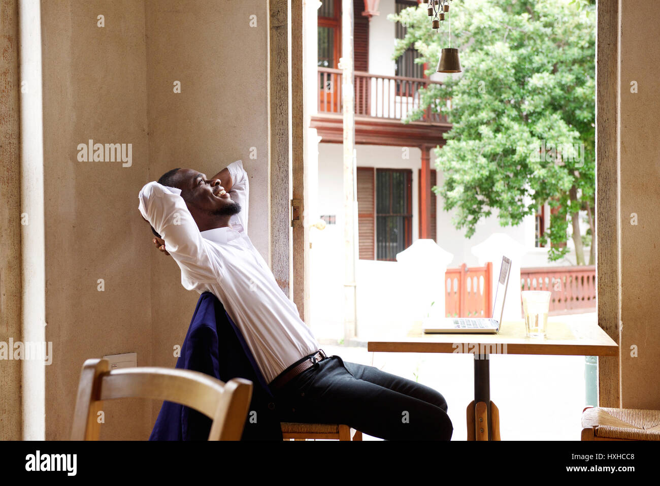 Ritratto di un imprenditore sorridente seduto presso il cafe con le mani dietro la testa Foto Stock
