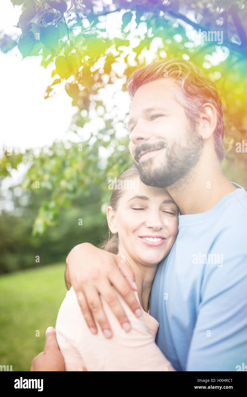 Coppia giovane in amore abbracciando in giardino con rainbow come dating agency annuncio Foto Stock
