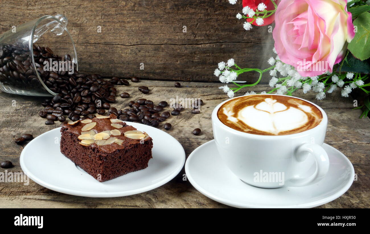 Cappuccino caffè e dolce brownie al cioccolato torta. Una tazza di latte, cappuccino o un espresso con il latte su un tavolo in legno scuro con la tostatura i chicchi di caffè. Foto Stock
