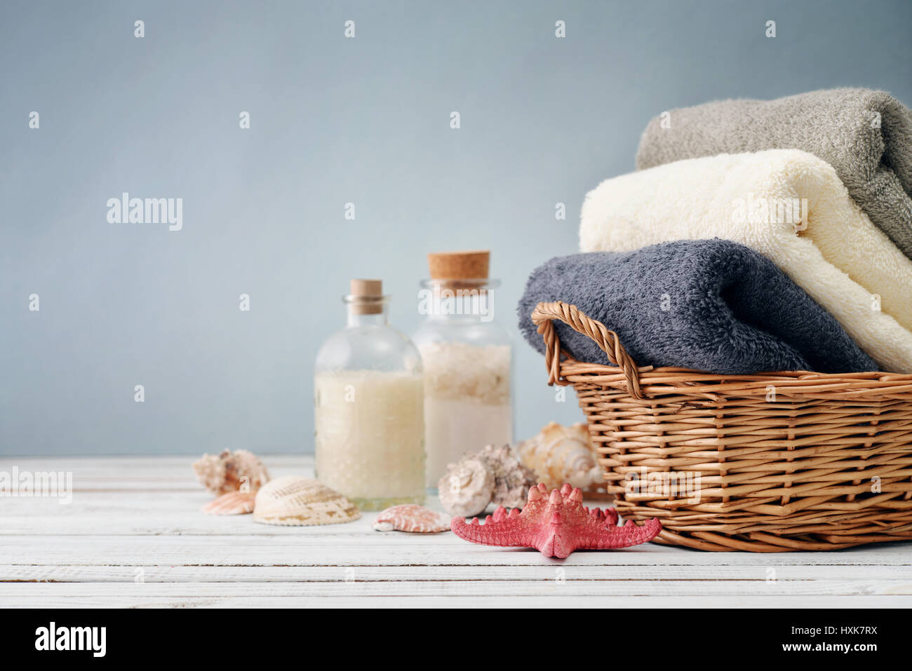 Asciugamani da bagno di colori diversi nel cesto di vimini con conchiglie di mare su sfondo chiaro Foto Stock