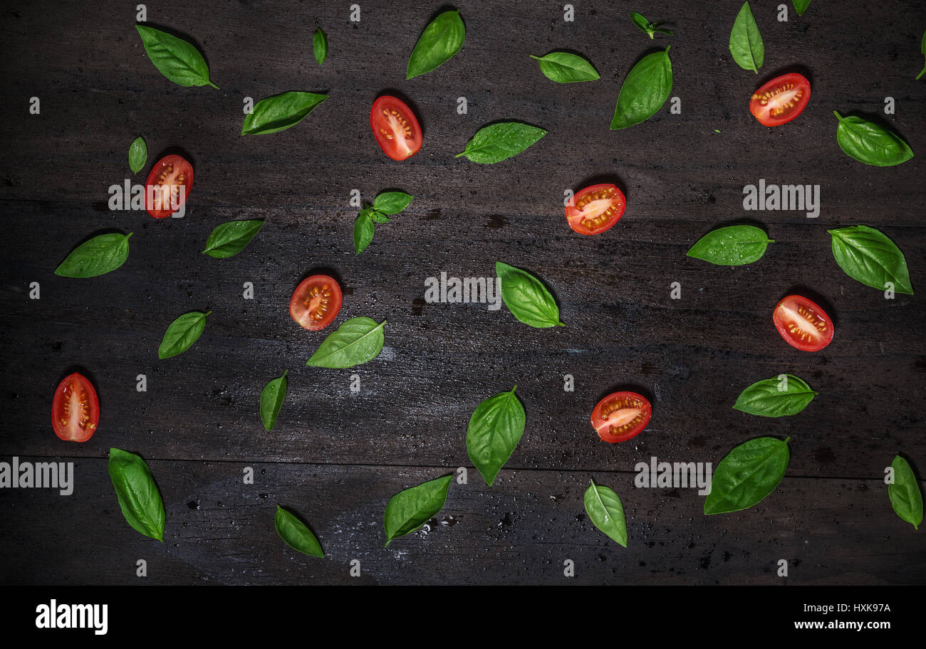 Le foglie di basilico e i pomodori su un vecchio nero lo sfondo in legno.Vista Superiore Foto Stock