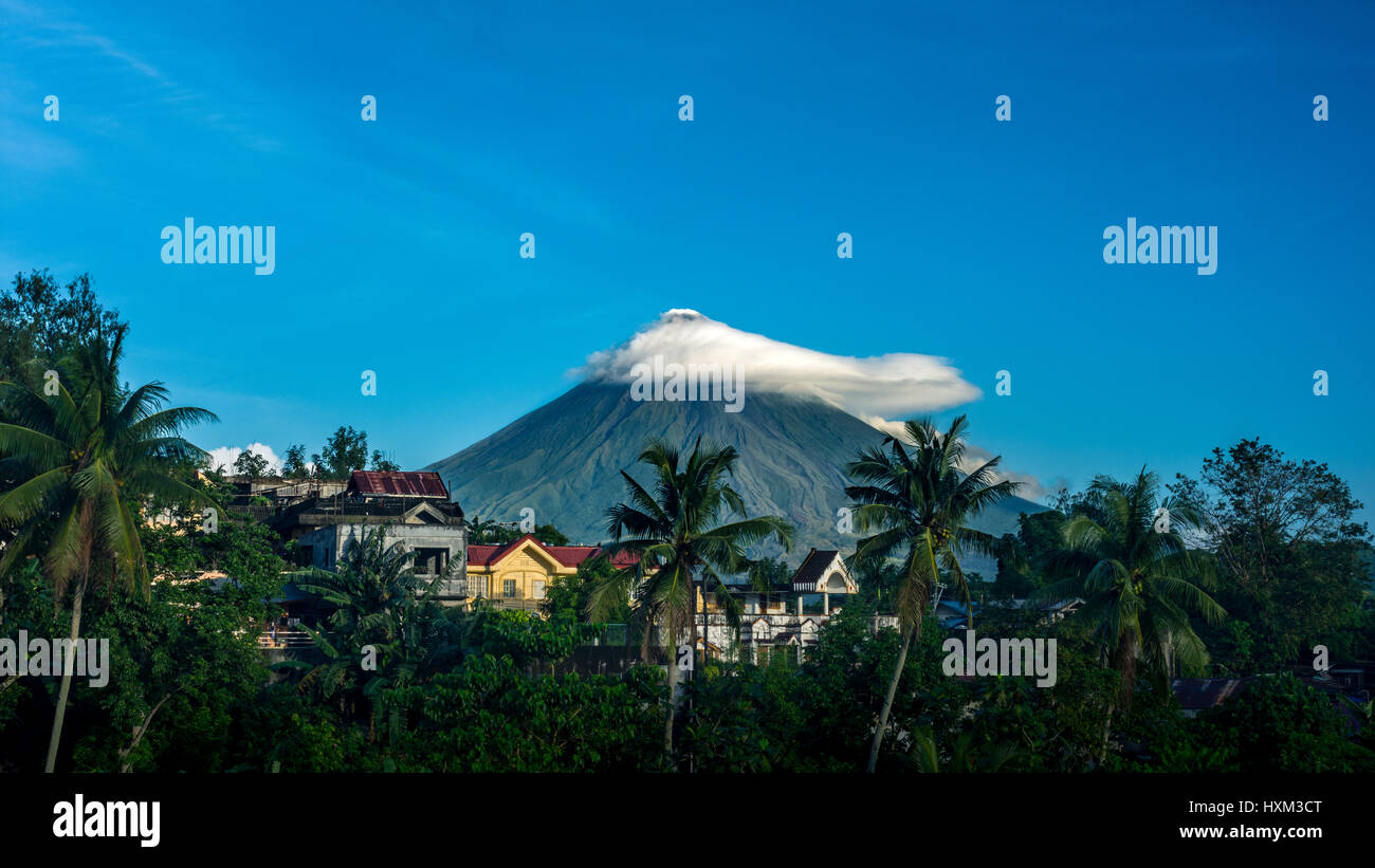 Vista in lontananza Vulcano Mayon, Legazpi, Filippine con piccole nuvole con case e alberi di palma in avanti la massa. Foto Stock