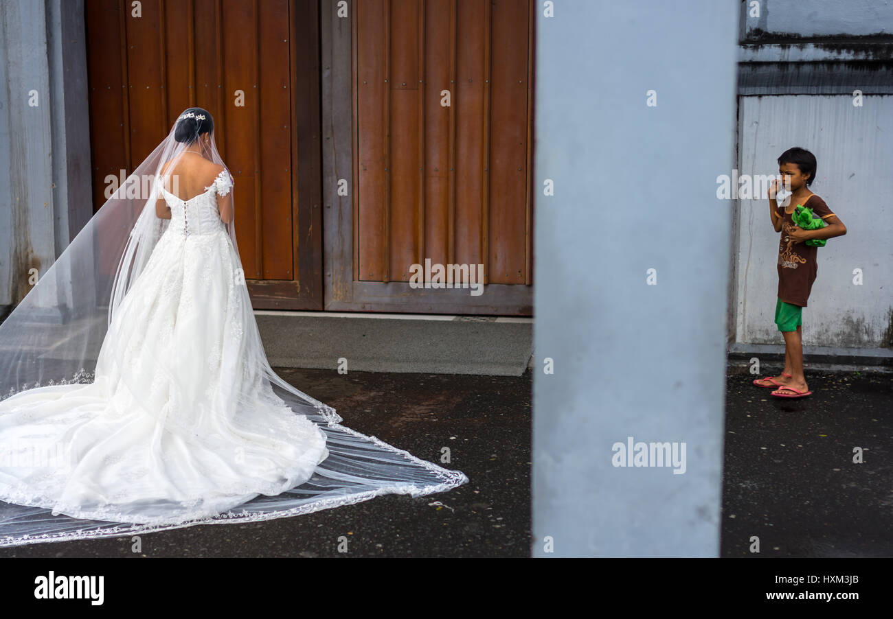 Una povera ragazza di strada bambino orologi e ammira le donne come sposa in un grande bianco abito da sposa attende presso la porta della chiesa. Foto Stock