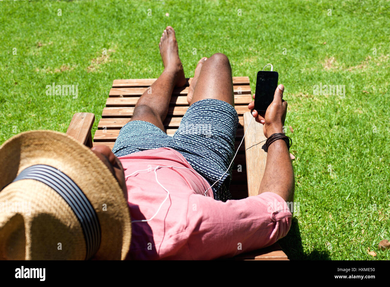 Ritratto di uomo disteso sulla sedia a sdraio in possesso di un telefono cellulare in un giorno di estate Foto Stock