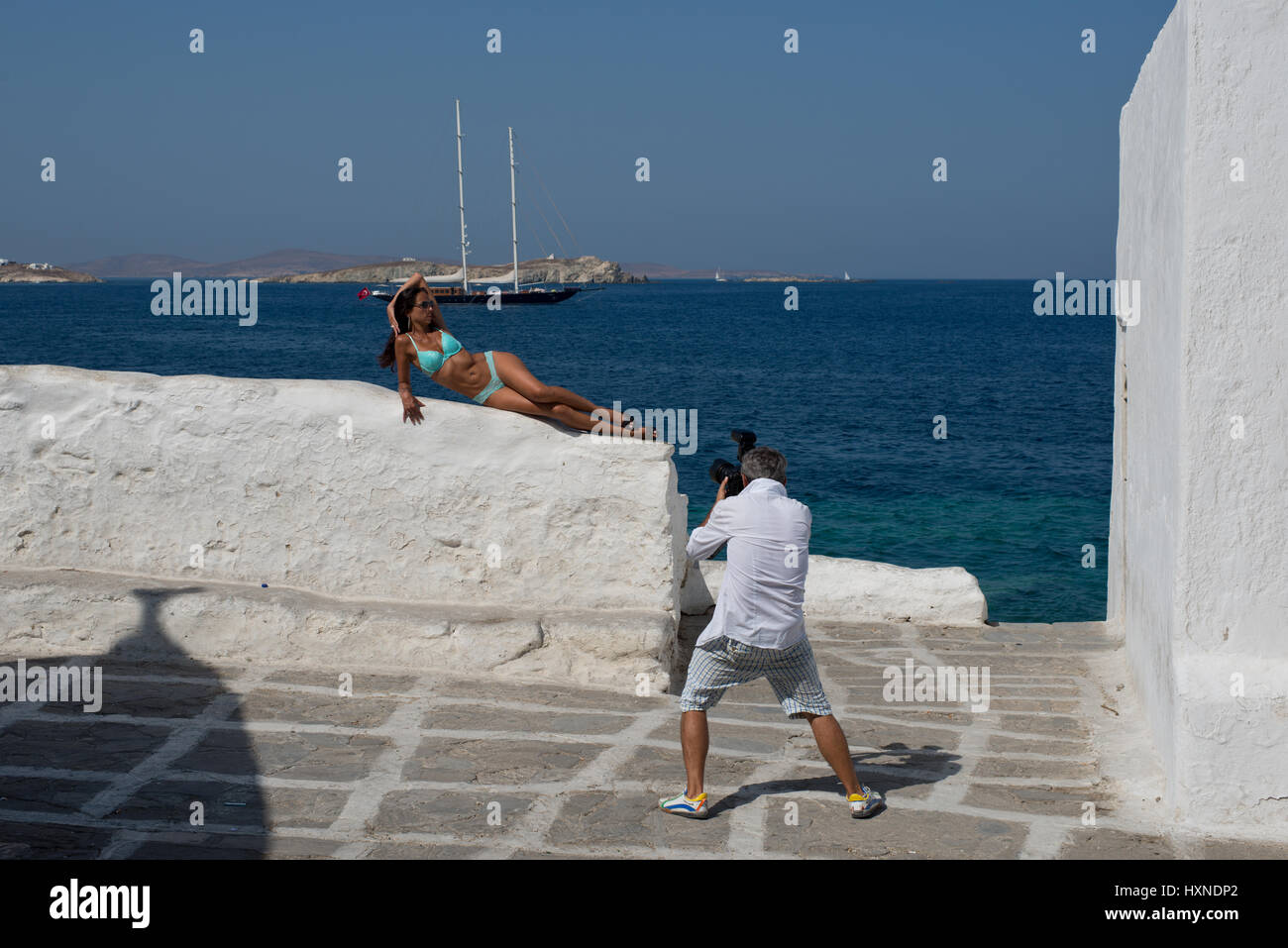 Fotografo scatta le foto di una donna in bikini sulla parete dipinta di bianco vicino a waterfront a Mykonos, Grecia Foto Stock