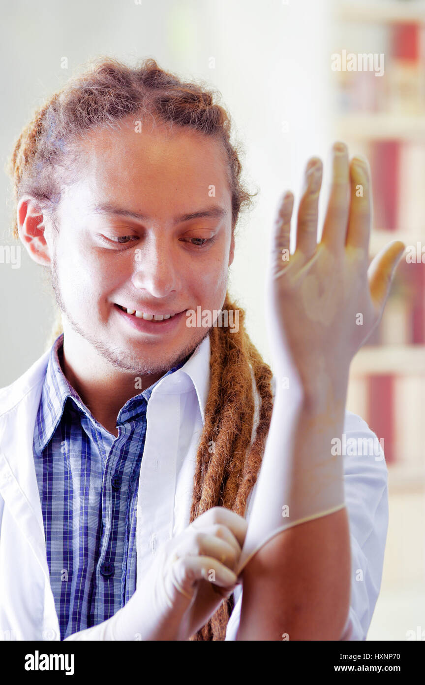Giovane medico con lunghi dread si blocca in posa per la telecamera mentre mettere dei guanti di gomma, clinica in background, concetto medico Foto Stock