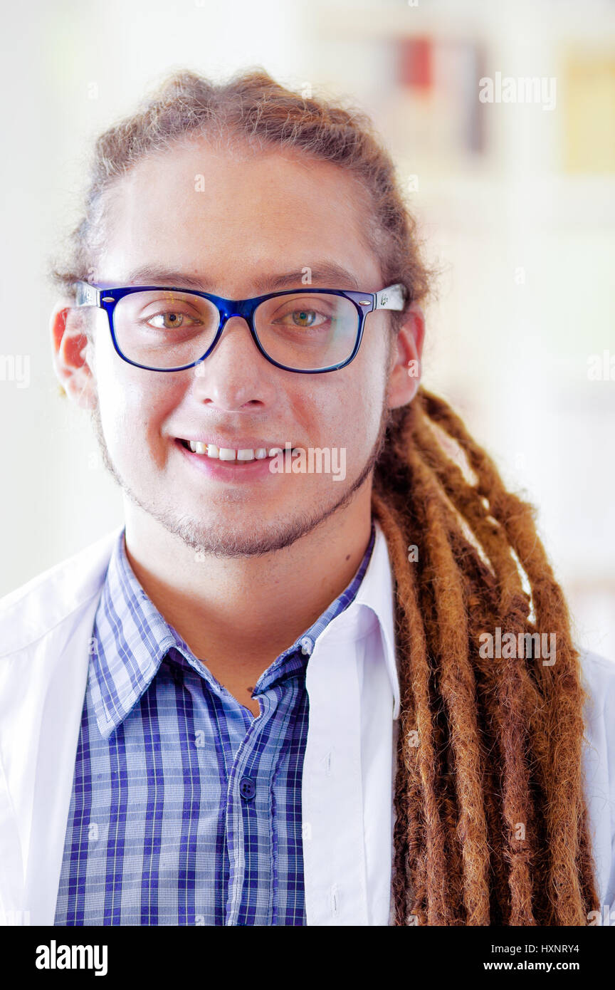 Giovane medico con lunghi dread si blocca in posa per la telecamera mentre sorridente, clinica in background, concetto medico Foto Stock