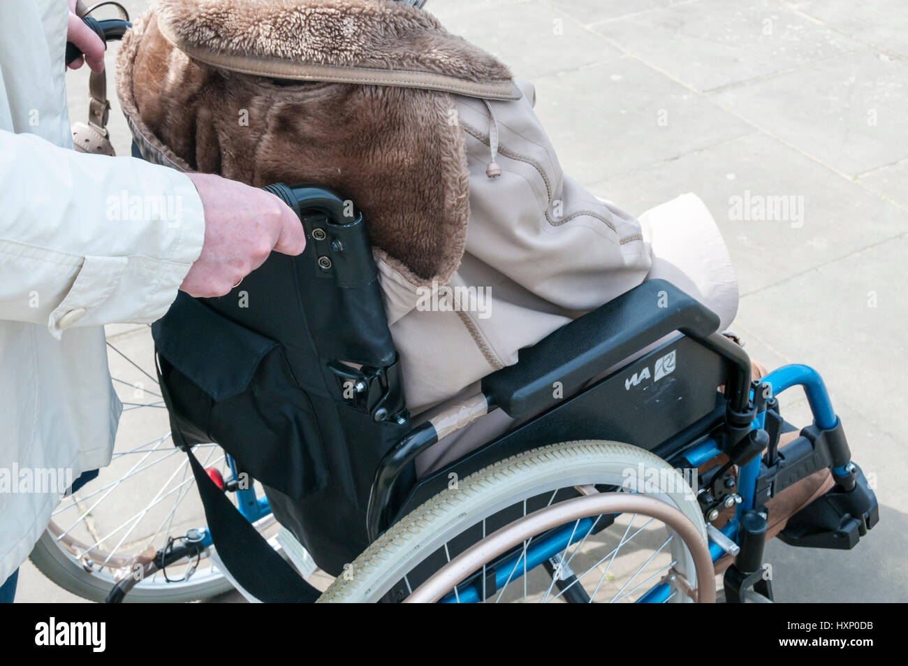 Signora anziana in carrozzella essendo spinta da un accompagnatore o assistente. Foto Stock
