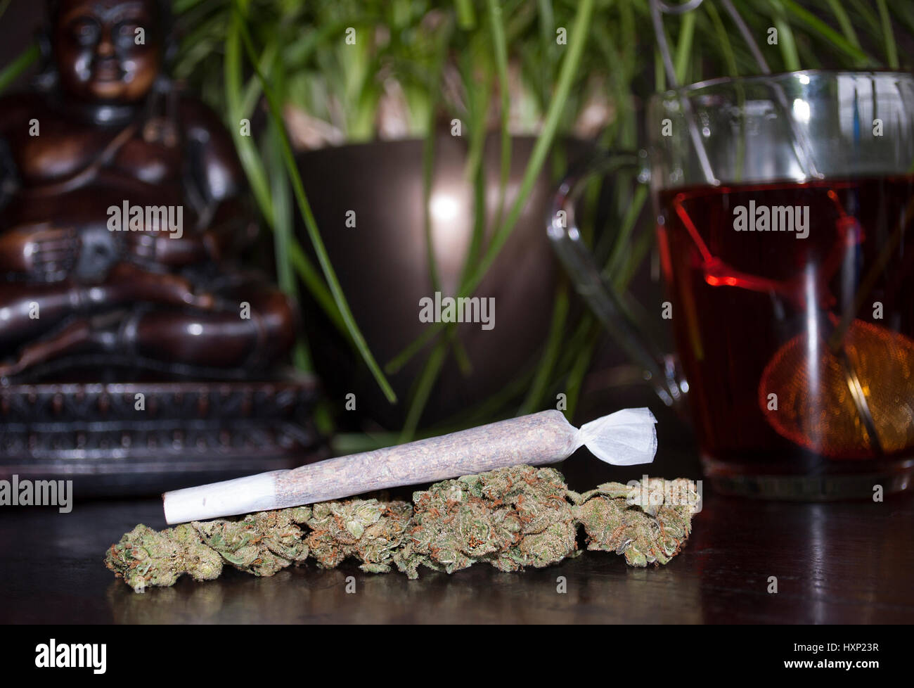 Primo piano della marijuana laminati giunto di erbaccia e gemme su sfondo di legno, con la statuetta di Buddha e la tazza di tè rooibos Foto Stock