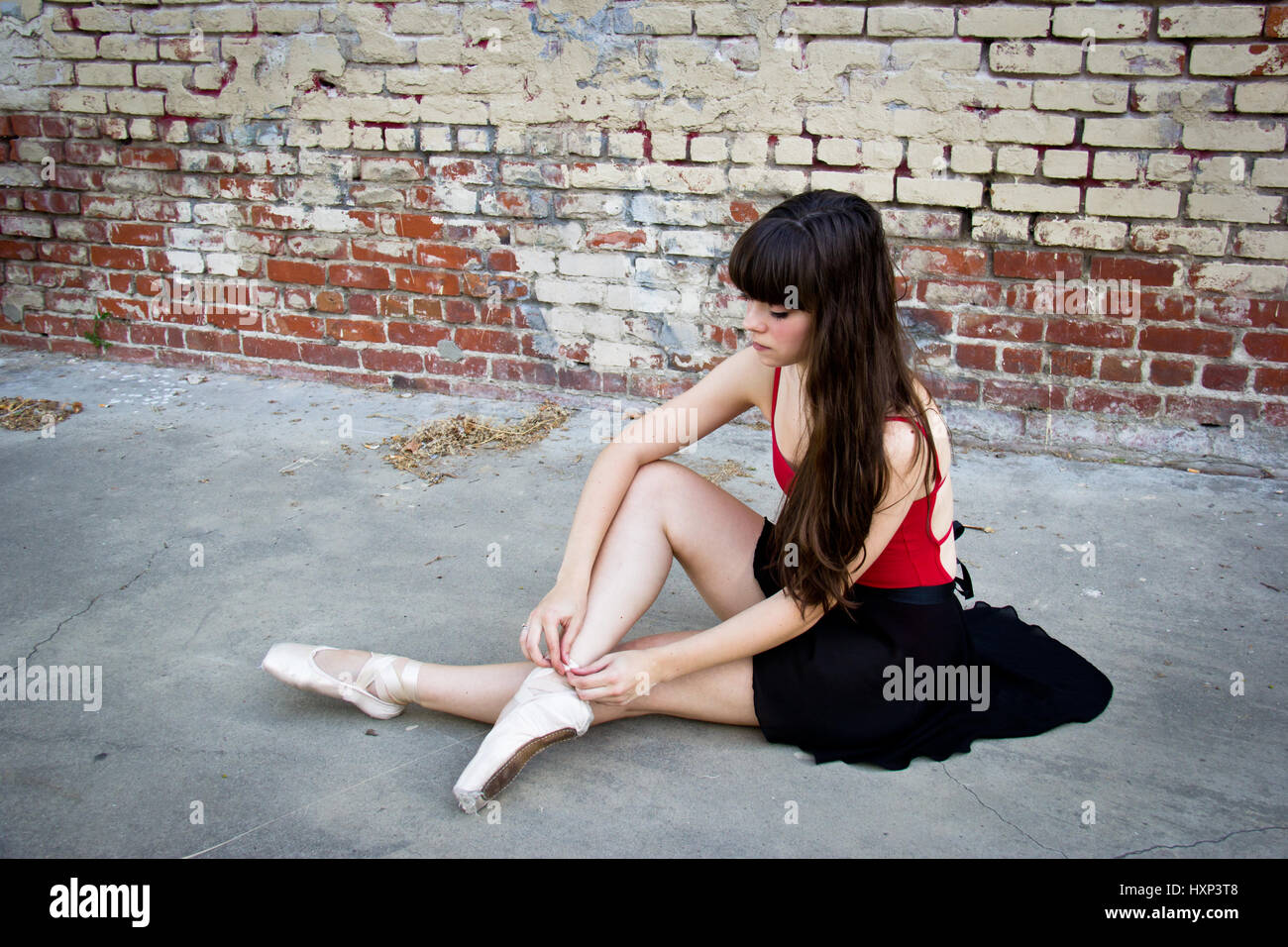 Bruna giovane ballerina seduta in un vicolo a mettere su il suo punto scarpe. Foto Stock