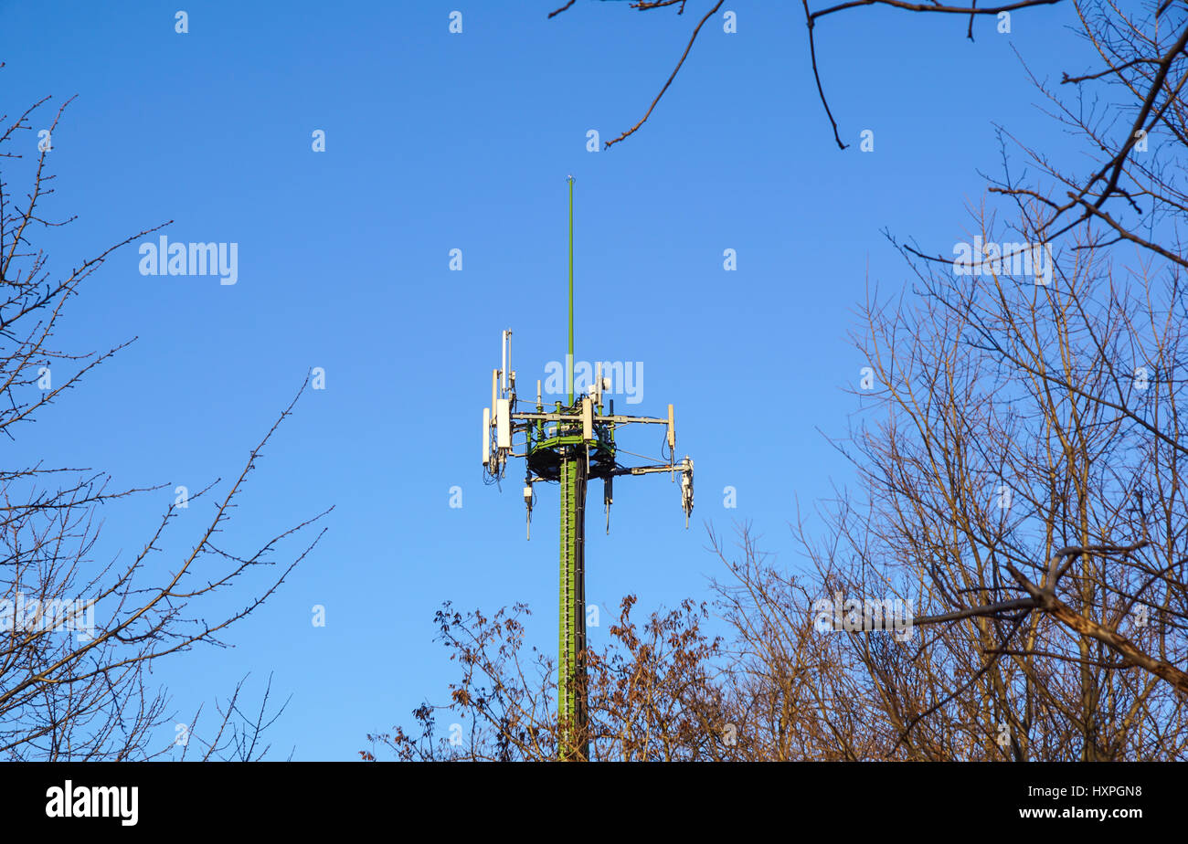 Acciaio torre di telecomunicazione con le antenne sul cielo blu e alberi Foto Stock