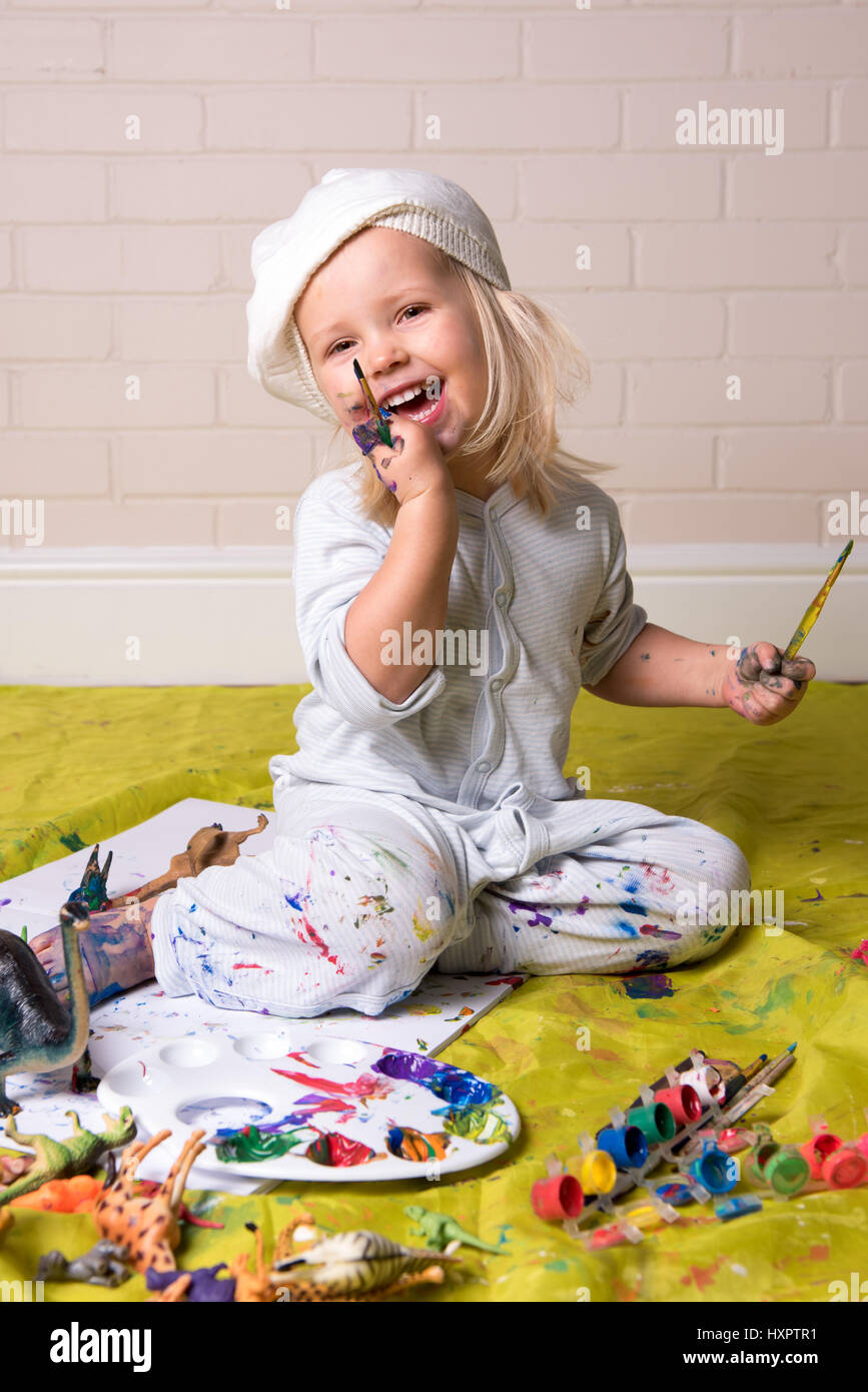 Felice bambina aventi gioco disordinato e guardando la telecamera mentre la pittura. Divertente l'infanzia. Foto Stock