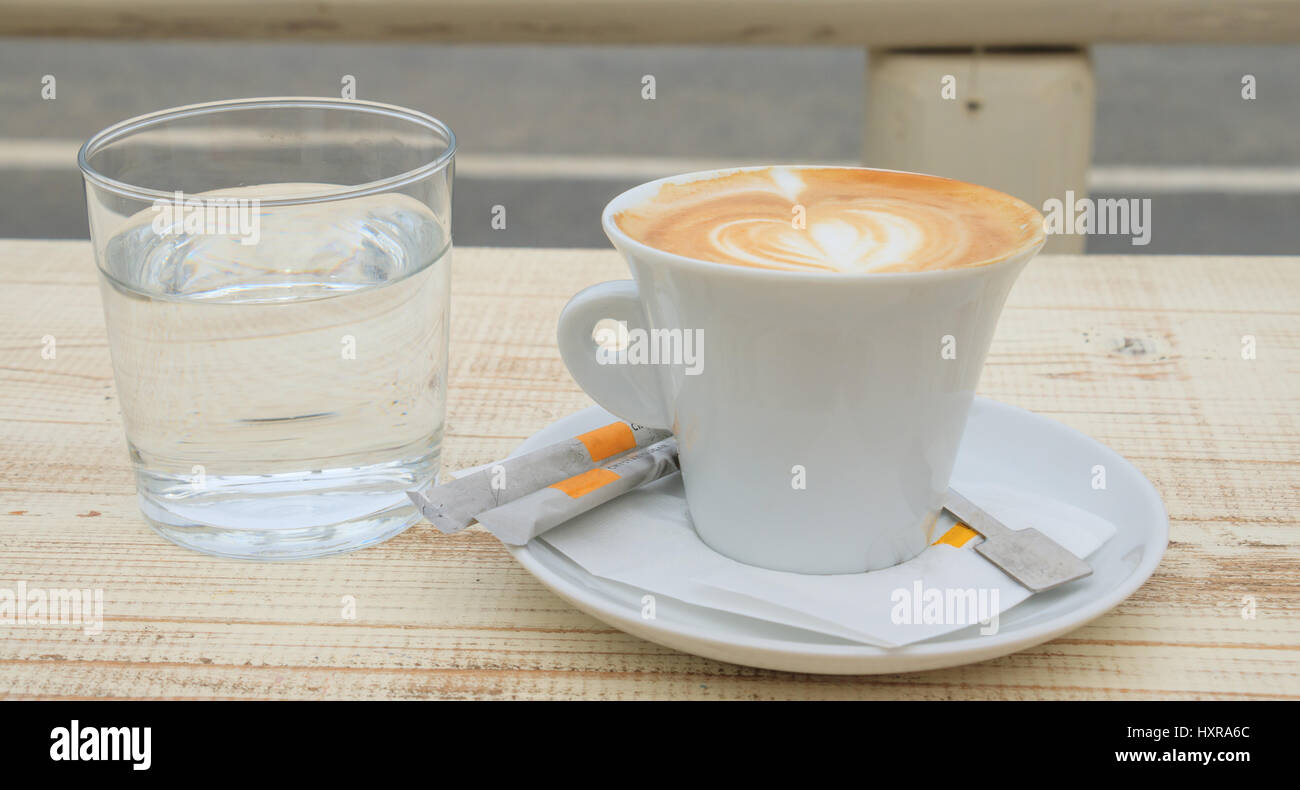 Tazza di cappuccino e un bicchiere di acqua su un tavolo di legno Foto Stock