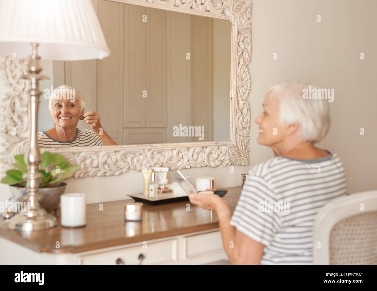 Sorridente donna senior di applicare il trucco in uno specchio a casa Foto Stock