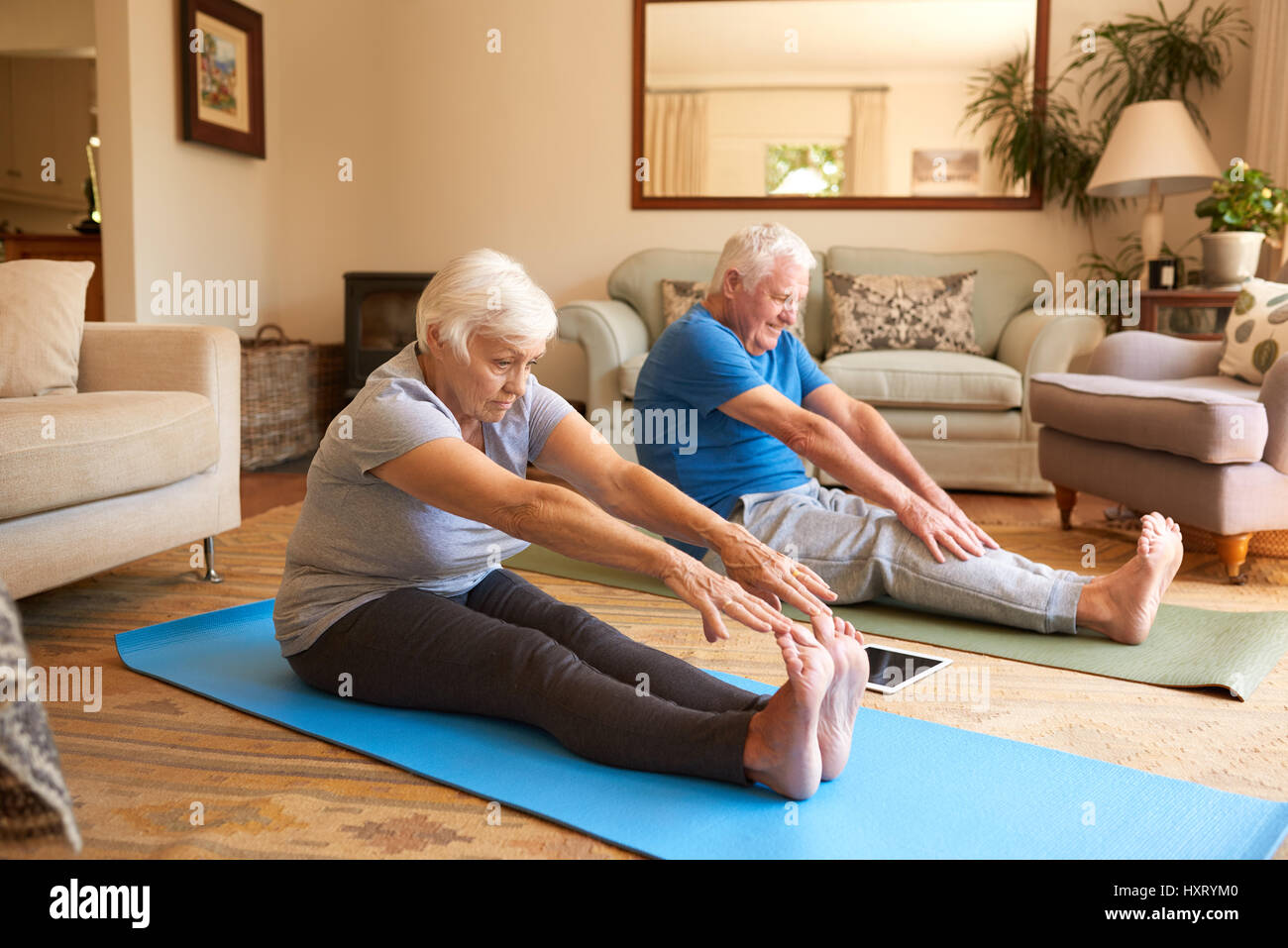 Attivo coppia senior stretching insieme mentre fare yoga a casa Foto Stock