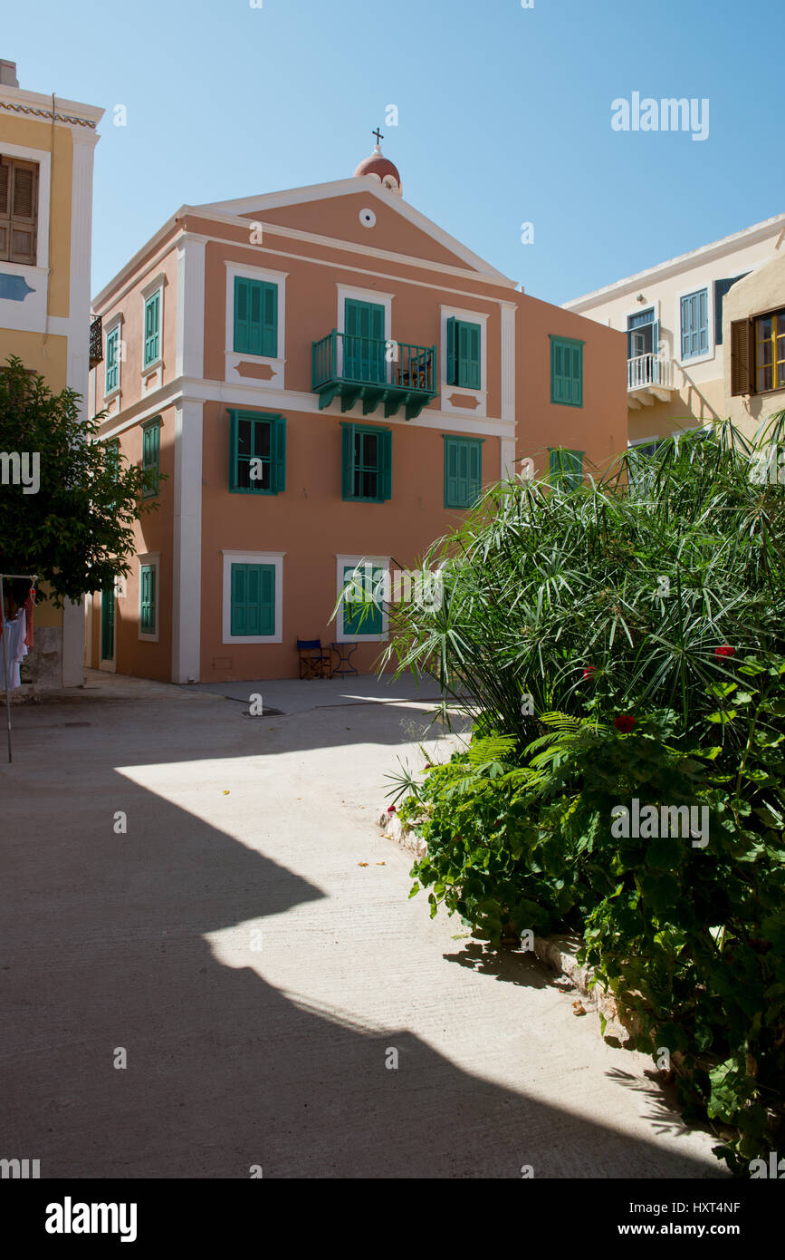 Orangefarbenes Haus mit grünen Fensterläden auf Dorfplatz, rechts Grünpflanzen, Insel Kastellorizo, Dodekanes, Griechenland Foto Stock