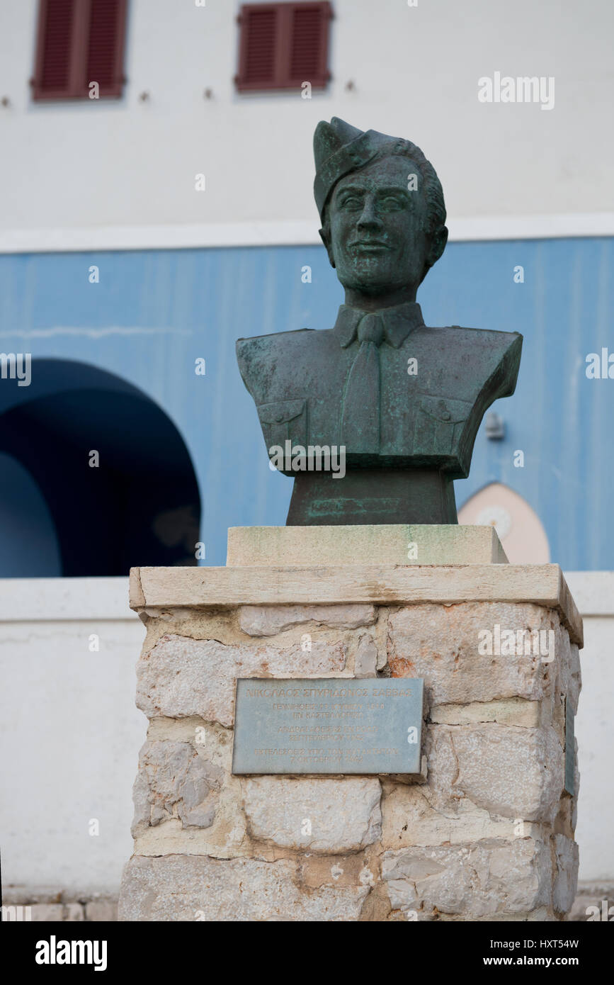 Brustbild- monumento in bronzo eines Soldaten auf Steinsockel, im Hintergrund blau-weißes Haus, rote Fenster, Insel Kastellorizo, Dodekanes, Griechenland Foto Stock