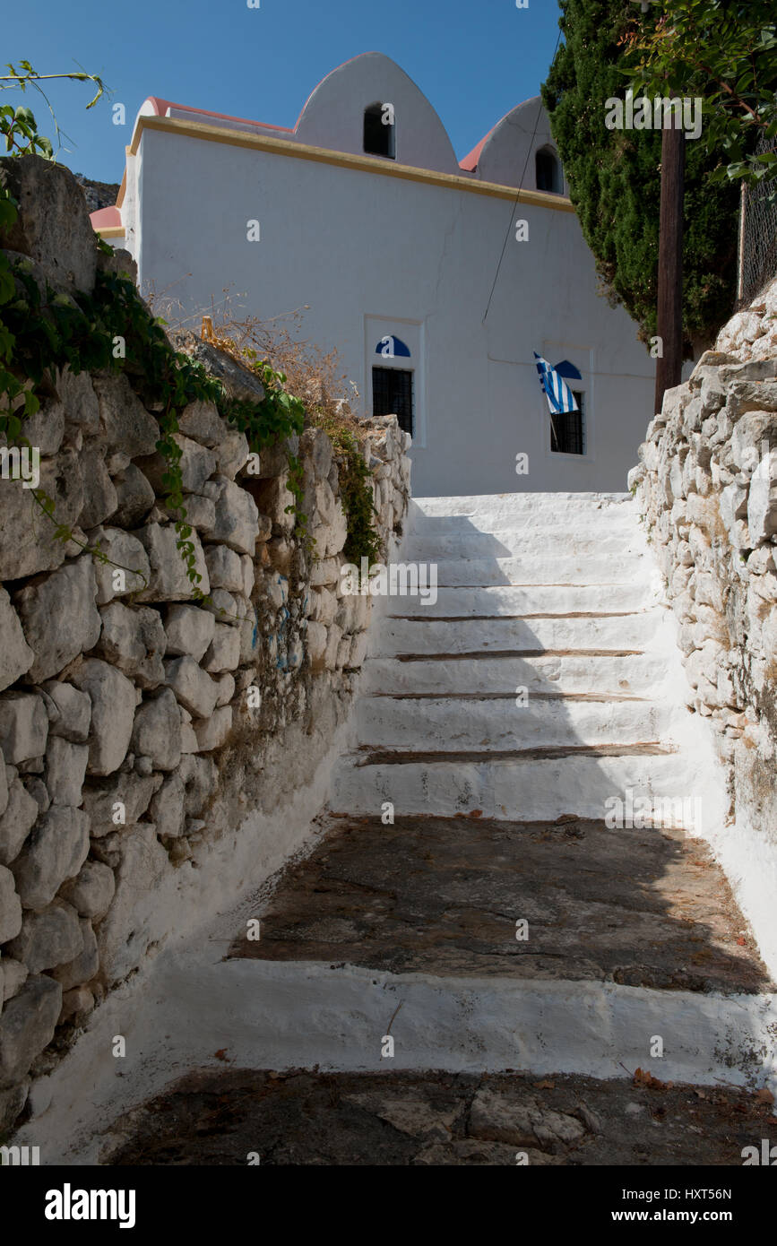 Weißbemalter Treppenaufgang mit seitlichen Steinmauern und weißer Kirche mit griechischer Fahne, Insel Kastellorizo, Dodekanes, Griechenland Foto Stock