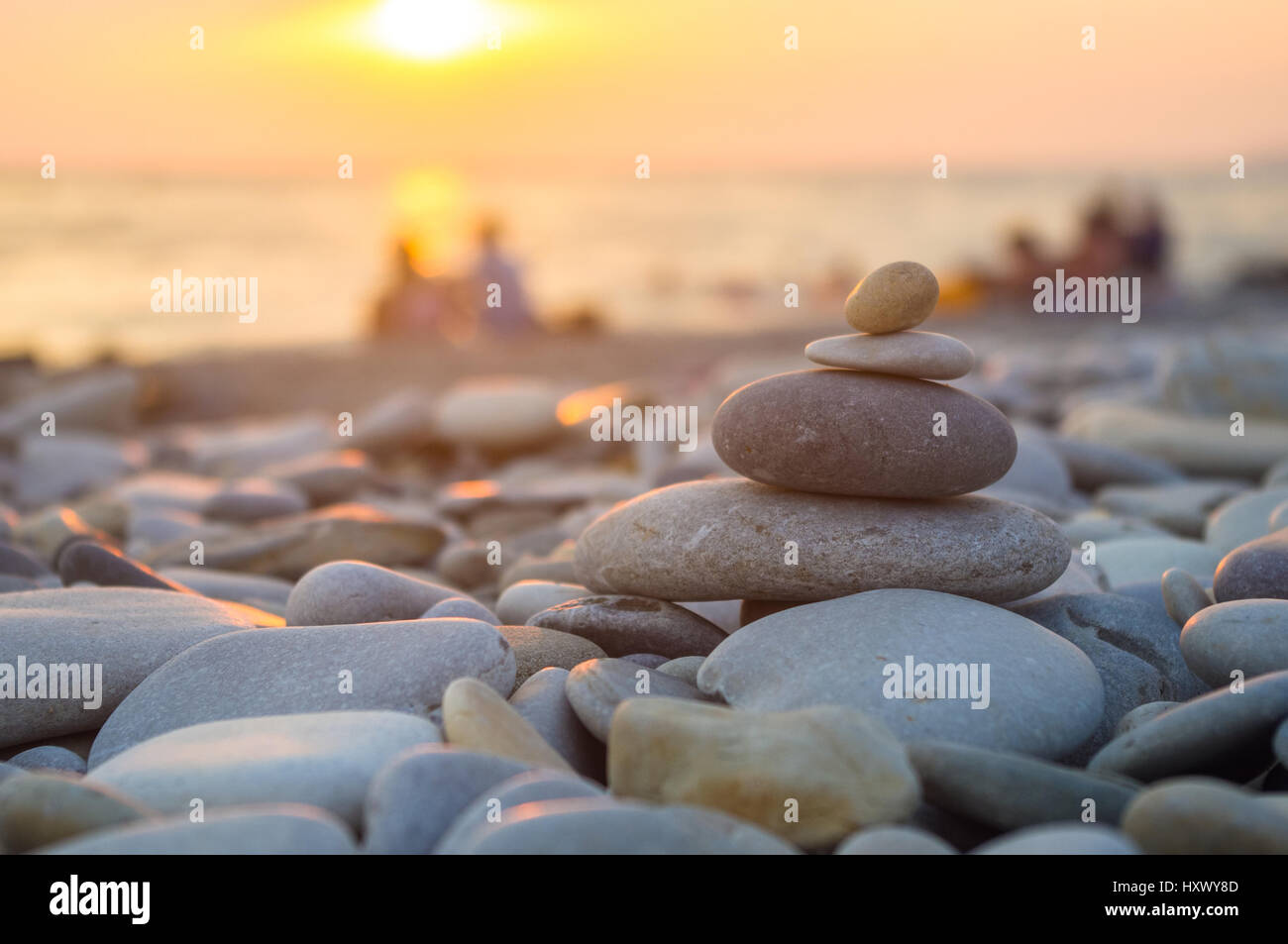 Un giovane e ripiegati a piramide Zen pietre ghiaia sul mare spiaggia al tramonto Foto Stock