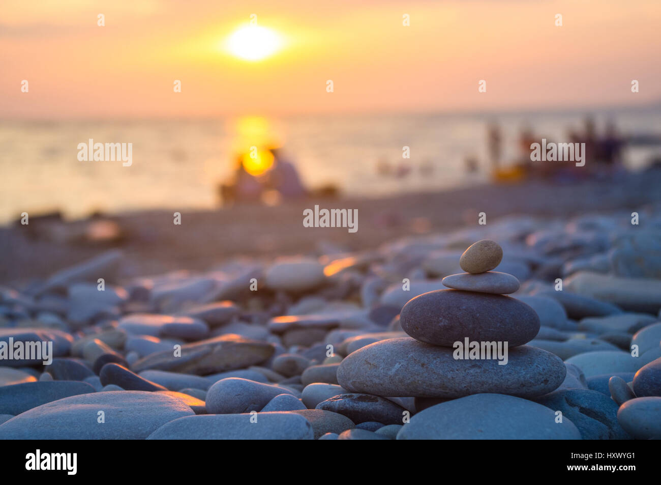 Un giovane e ripiegati a piramide Zen pietre ghiaia sul mare spiaggia al tramonto Foto Stock