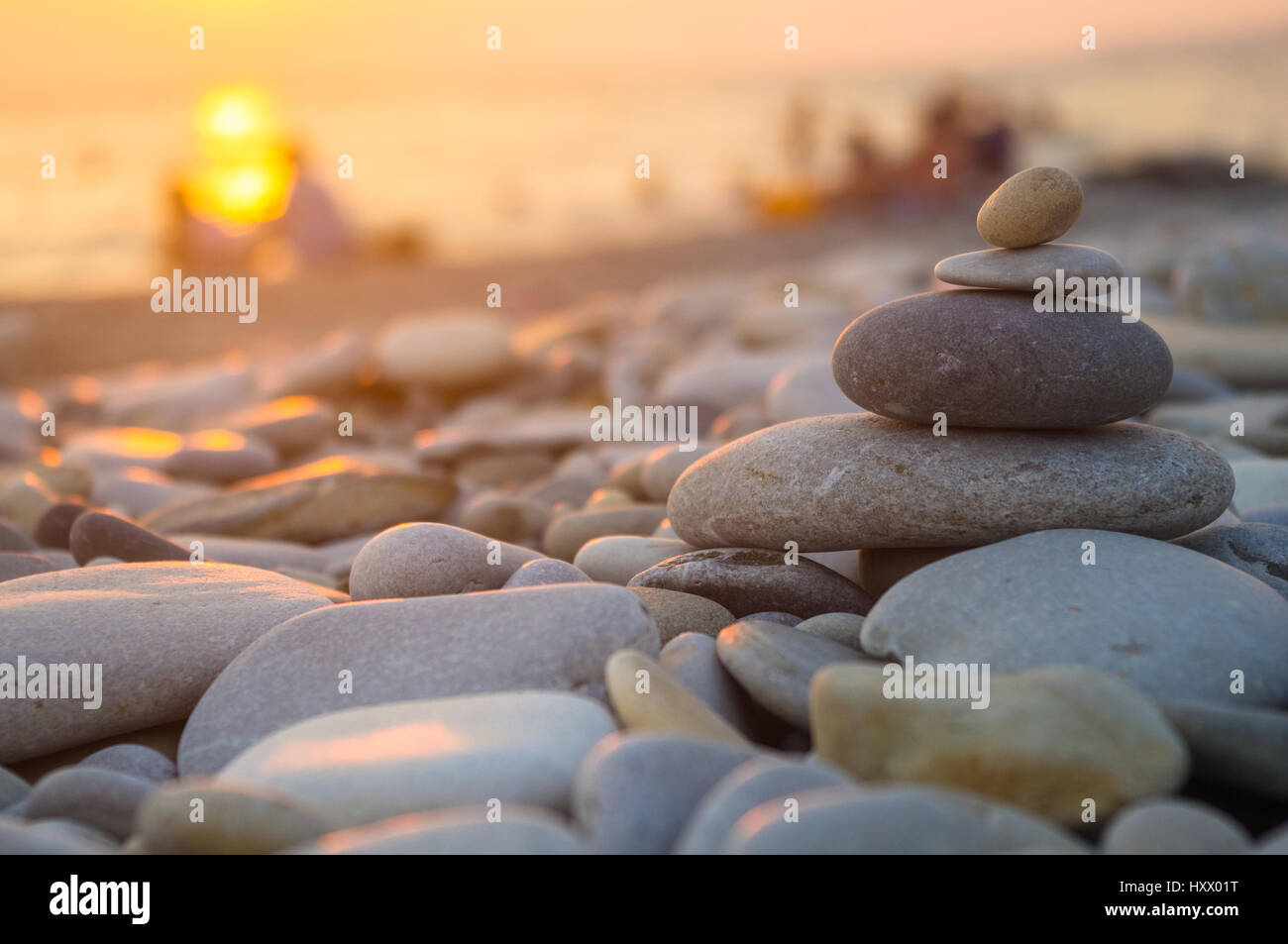 Un giovane e ripiegati a piramide Zen pietre ghiaia sul mare spiaggia al tramonto Foto Stock